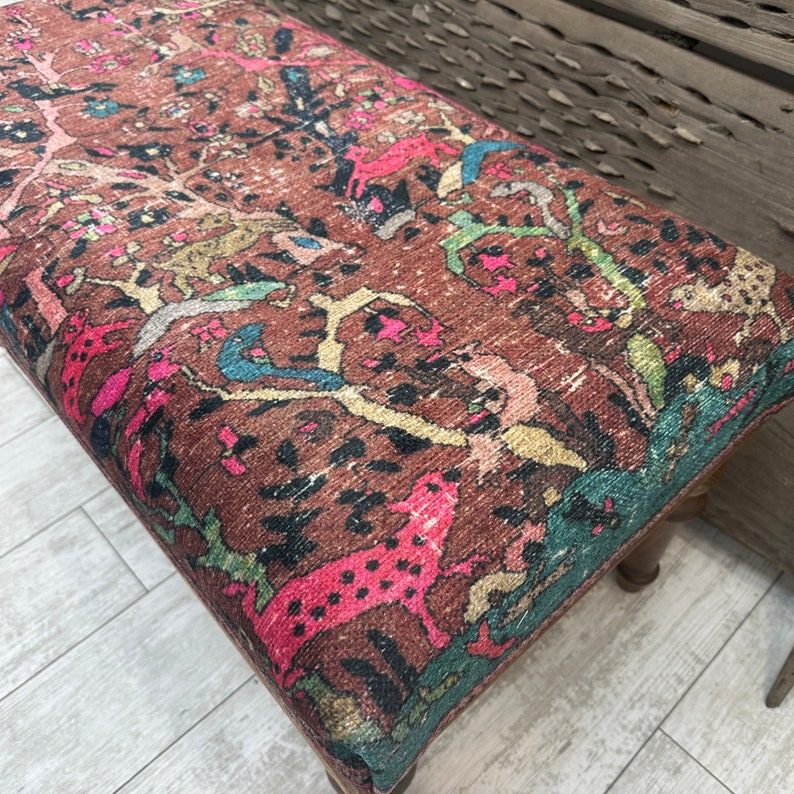 Peut inclure: Un ottoman &agrave; motifs color&eacute;s avec une base brune. Le tissu pr&eacute;sente un motif r&eacute;p&eacute;titif d'animaux et de plantes dans des tons de rose, bleu, vert et jaune.