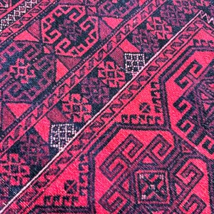 May include: Close-up of a red and black patterned rug. The rug features geometric designs and a repeating pattern. The dominant color is red, with black accents creating contrast. The rug's texture appears soft and woven.