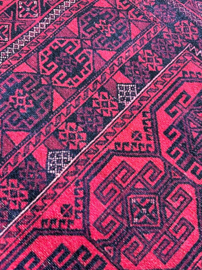 May include: Close-up of a red and black patterned rug. The rug features geometric designs and a repeating pattern. The dominant color is red, with black accents creating contrast. The rug's texture appears soft and woven.