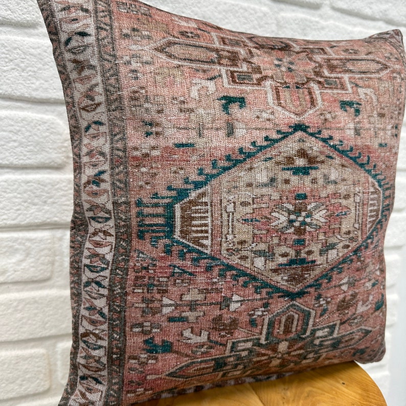 May include: A pink and teal patterned throw pillow with a geometric design. The pillow is made of a soft, woven fabric and has a subtle distressed look.