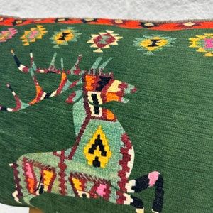 May include: Green cushion with a colourful geometric deer design. The cushion has a red, orange, yellow, black and white geometric pattern.