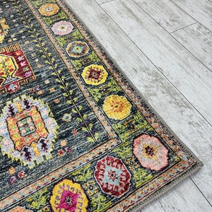 May include: A colorful rug with a geometric pattern in shades of green, yellow, pink, and red. The rug has a dark gray background and a fringe border.