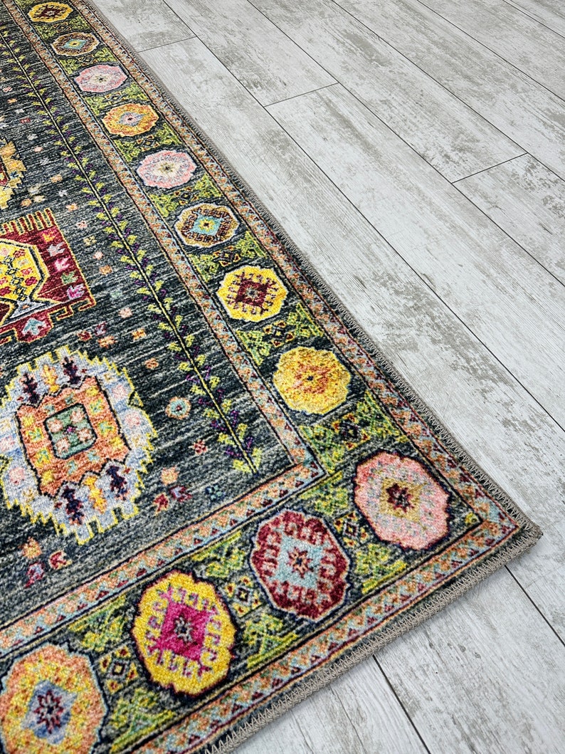 May include: A colorful rug with a geometric pattern in shades of green, yellow, pink, and red. The rug has a dark gray background and a fringe border.