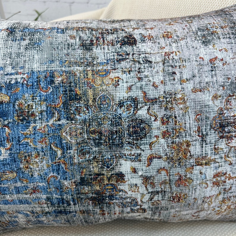May include: A decorative throw pillow with a blue, gray, and gold patterned design. The pattern features intricate floral and geometric motifs.