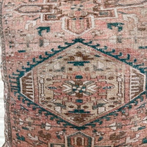 May include: A pink and teal patterned throw pillow with a geometric design. The pillow is made of a soft, woven fabric.