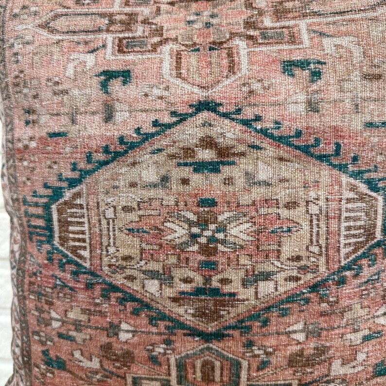 May include: A pink and teal patterned throw pillow with a geometric design. The pillow is made of a soft, woven fabric.