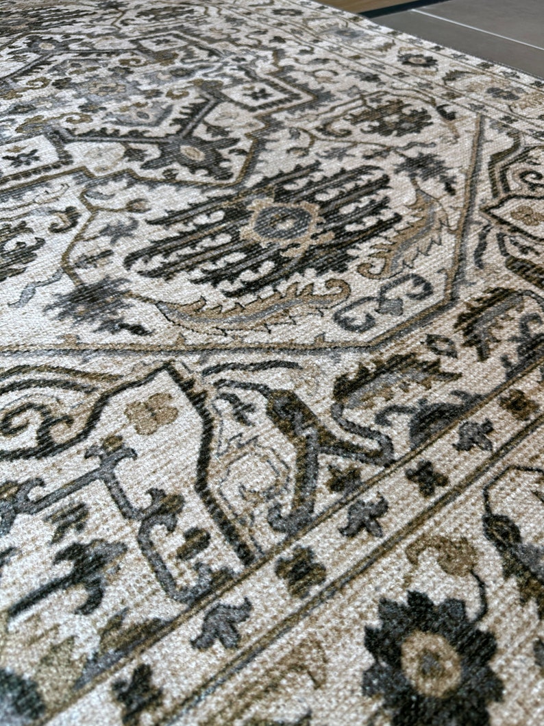 May include: A close-up of a beige rug with a detailed black and gray patterned design. The rug has a woven texture and a traditional style.