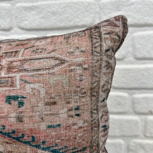May include: A close-up of a pink and brown patterned throw pillow with a teal and white geometric design. The pillow is made of a soft, woven fabric.
