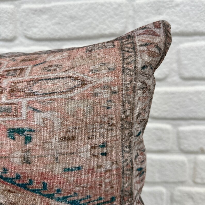 May include: A close-up of a pink and brown patterned throw pillow with a teal and white geometric design. The pillow is made of a soft, woven fabric.