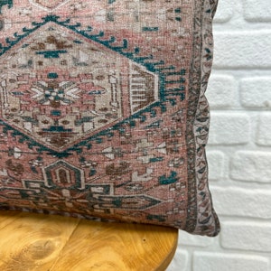 May include: A pink and teal patterned throw pillow with a fringed edge. The pillow is sitting on a wooden chair.
