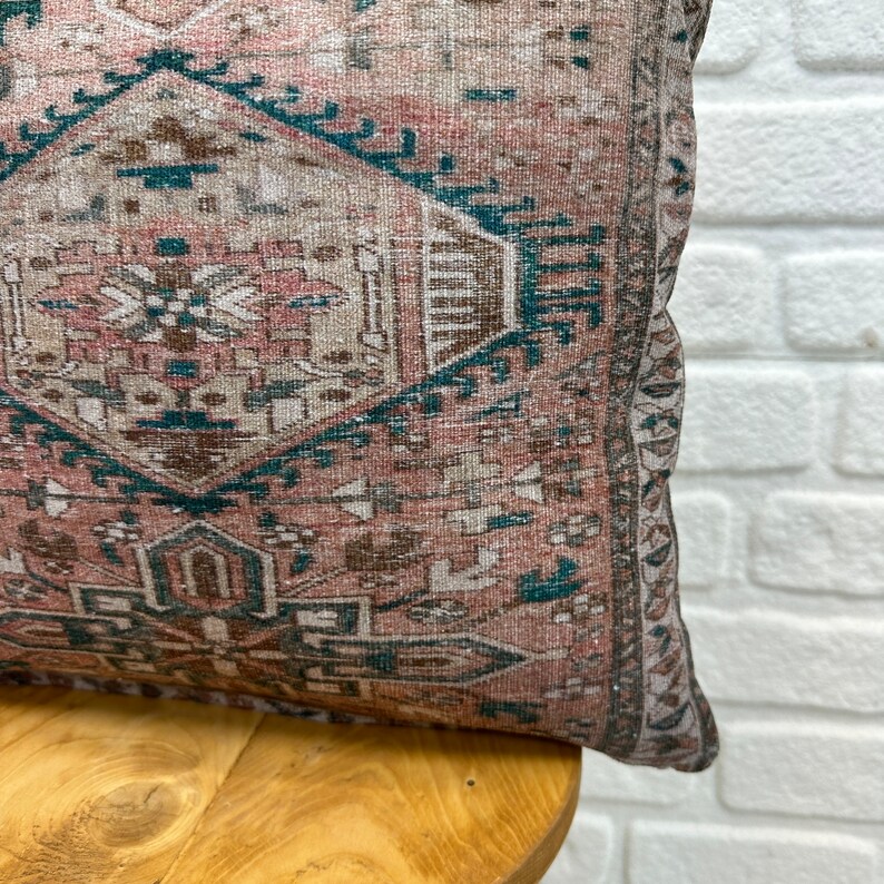 May include: A pink and teal patterned throw pillow with a fringed edge. The pillow is sitting on a wooden chair.