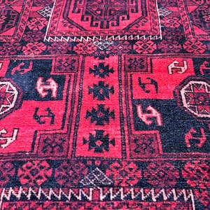 May include: Close-up of a red and black patterned rug. The rug features geometric designs and borders in black against a red background. The rug's texture is visible, suggesting a woven or knotted construction.