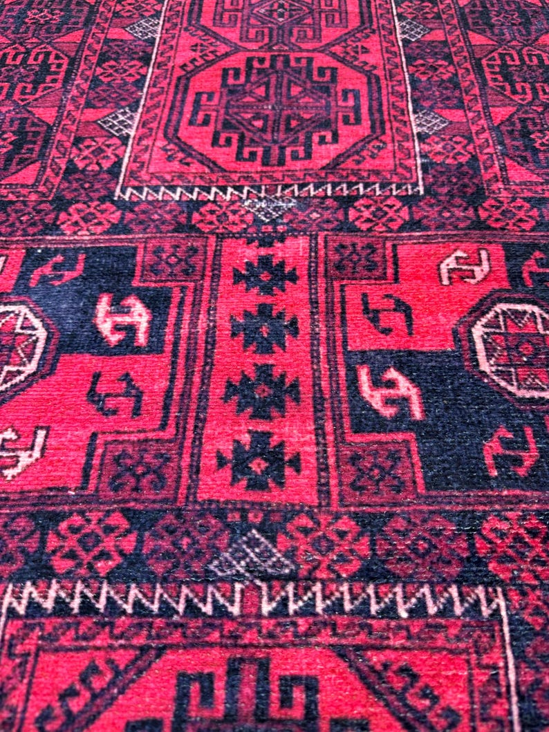 May include: Close-up of a red and black patterned rug. The rug features geometric designs and borders in black against a red background. The rug's texture is visible, suggesting a woven or knotted construction.