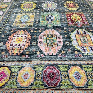 May include: A dark green rug with a colorful geometric pattern. The rug has a border with a floral design. The rug is made of wool and is hand-woven.