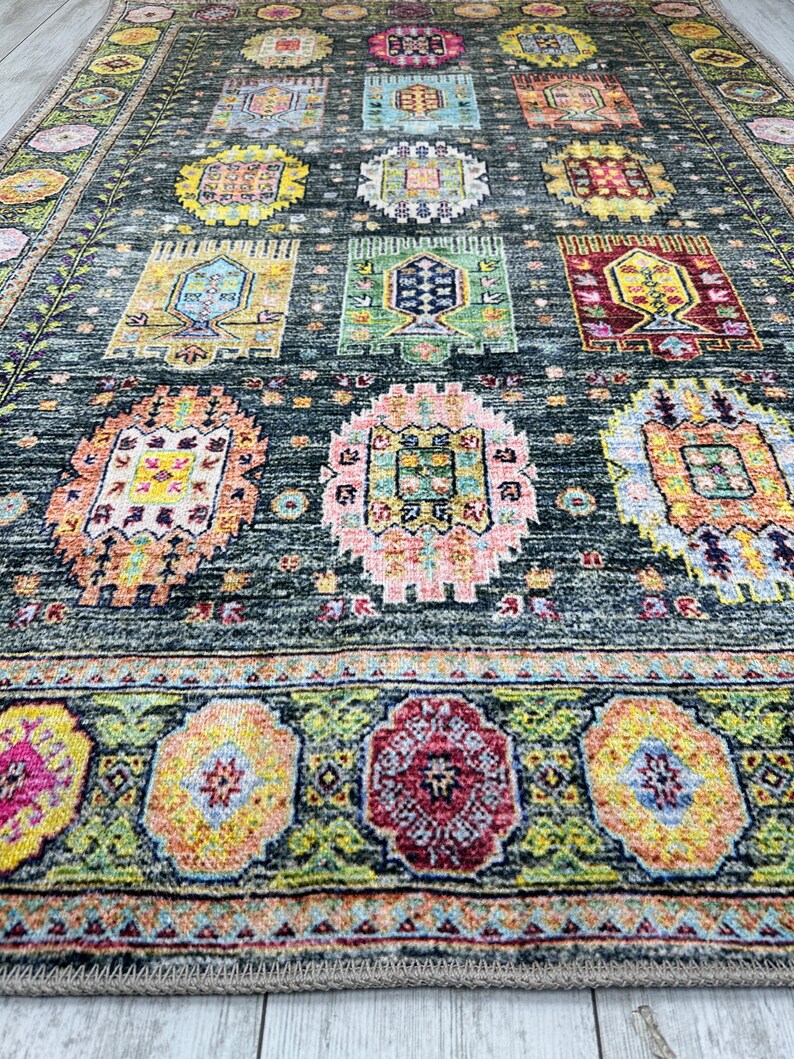 May include: A dark green rug with a colorful geometric pattern. The rug has a border with a floral design. The rug is made of wool and is hand-woven.