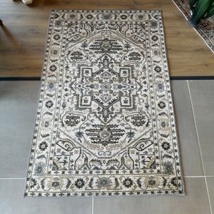 May include: A white rug with a black and gray geometric pattern. The rug has a border with a floral design.