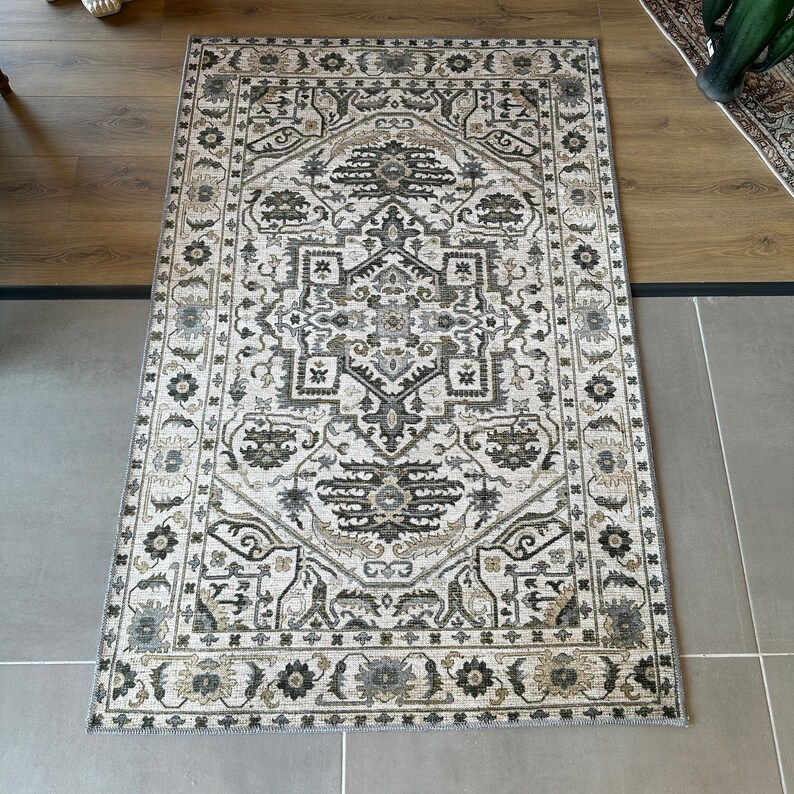 May include: A white rug with a black and gray geometric pattern. The rug has a border with a floral design.