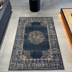 May include: A dark blue and cream patterned rug with a central medallion design. The rug has a distressed look and a fringed edge.