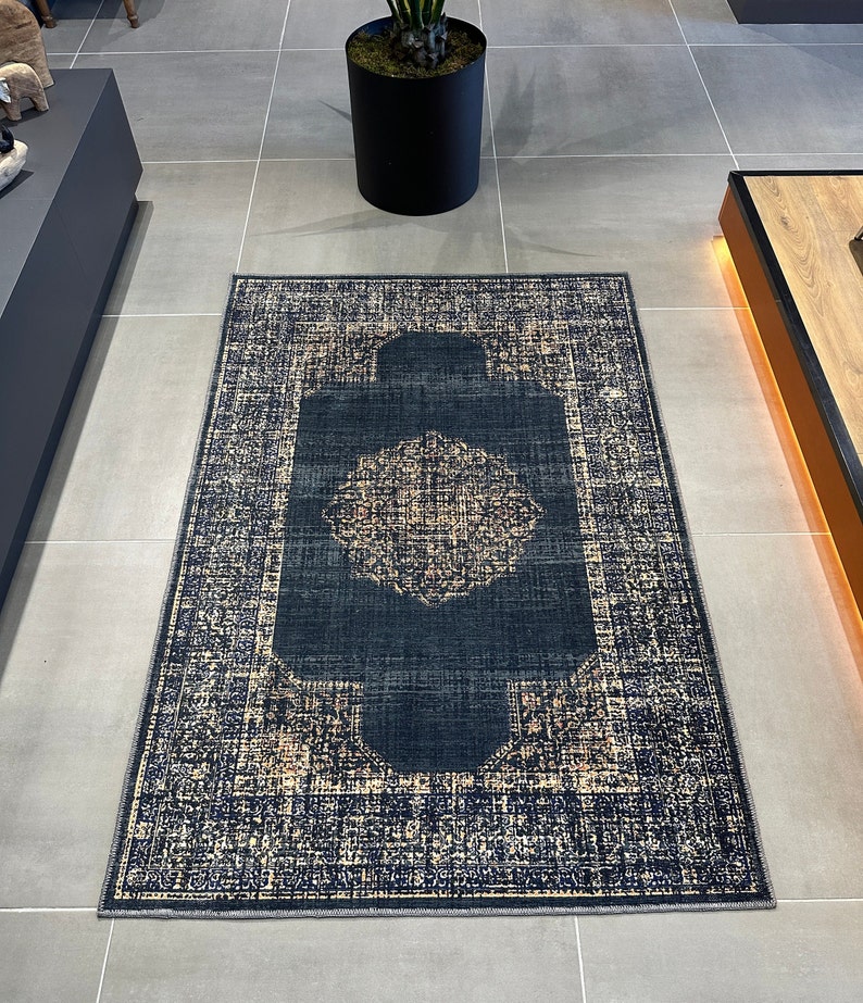May include: A dark blue and cream patterned rug with a central medallion design. The rug has a distressed look and a fringed edge.