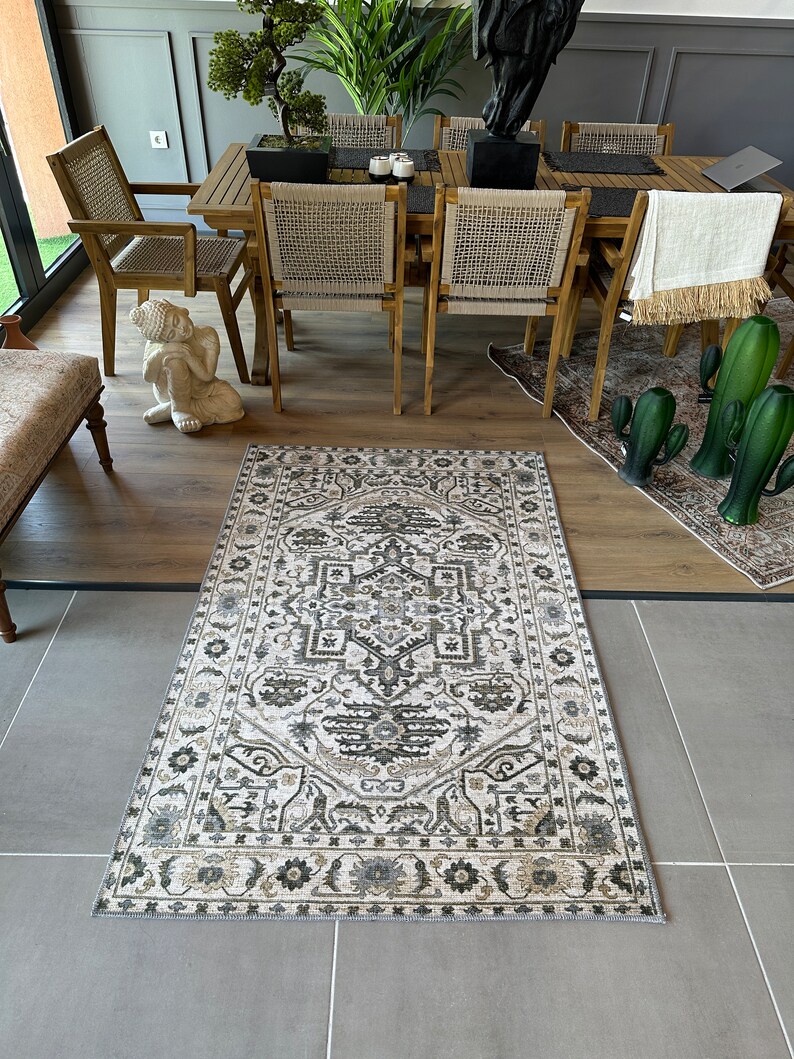 May include: A beige and brown patterned rug with a geometric design. The rug is laid out on a light gray tiled floor in a room with wooden furniture.