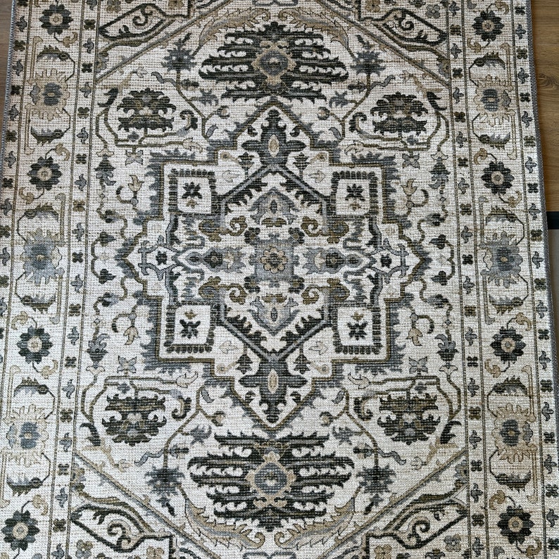 May include: A white rug with a black and gray geometric pattern. The rug has a traditional design with intricate details.
