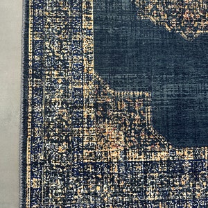 May include: Close-up of a dark blue rug with a patterned border in shades of gold, black, and blue. The rug has a distressed, vintage look.