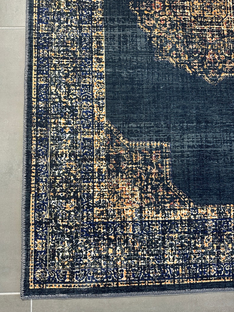 May include: Close-up of a dark blue rug with a patterned border in shades of gold, black, and blue. The rug has a distressed, vintage look.
