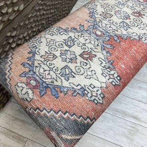 May include: A red, blue, and white patterned bench cushion with a geometric design. The cushion is made of a woven fabric and has a fringed edge.