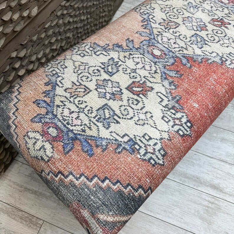 May include: A red, blue, and white patterned bench cushion with a geometric design. The cushion is made of a woven fabric and has a fringed edge.