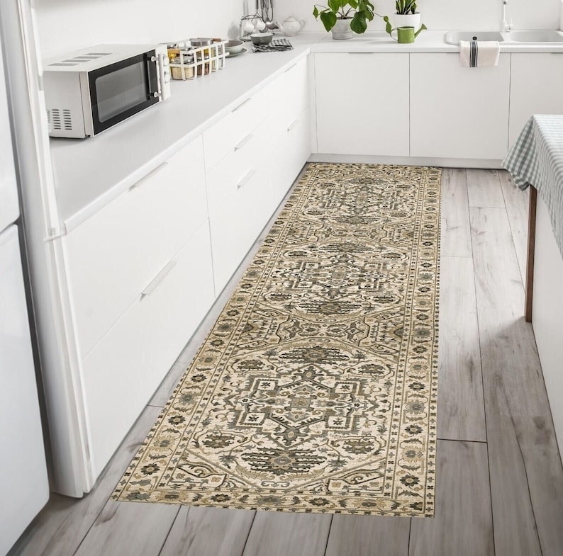 May include: A beige and brown patterned runner rug with a geometric design. The rug is placed in a kitchen with white cabinets and a wood floor.