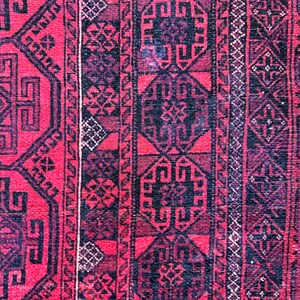 May include: Close-up of a red and black patterned rug. The rug features geometric designs and borders in shades of red, black, and dark purple. The intricate patterns create a textured appearance.