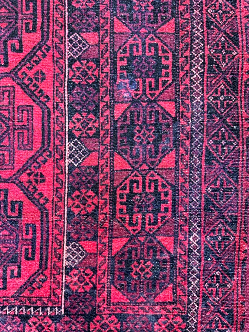 May include: Close-up of a red and black patterned rug. The rug features geometric designs and borders in shades of red, black, and dark purple. The intricate patterns create a textured appearance.