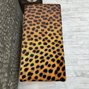 May include: Upholstered bench with a leopard print pattern in shades of brown, orange, and black. The rectangular bench has a padded top and is suitable for seating or as a decorative accent piece.