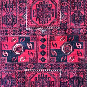 May include: A close-up of a red and black patterned rug. The rug features geometric designs, including octagonal shapes and repeating patterns. The color palette is dominated by deep red and black, with small white accents.