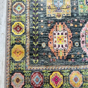 May include: A dark gray rug with a colorful geometric pattern. The rug has a border with a repeating design of flowers and leaves.