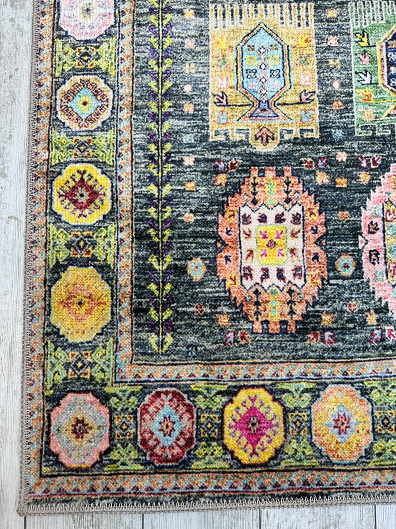 May include: A dark gray rug with a colorful geometric pattern. The rug has a border with a repeating design of flowers and leaves.