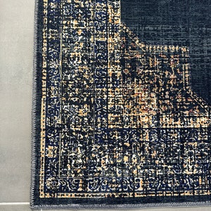 May include: Close-up of the edge of a dark blue rug with a detailed pattern in shades of gold and blue. The rug has a gray border.