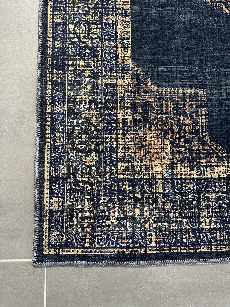 May include: Close-up of the edge of a dark blue rug with a detailed pattern in shades of gold and blue. The rug has a gray border.