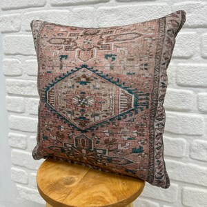 May include: A pink and teal patterned throw pillow with a geometric design. The pillow is made of a soft, woven fabric and has a fringed edge.