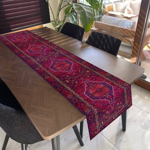 Könnte beinhalten: Ein roter und blauer Tischläufer mit geometrischem Muster. Der Läufer liegt auf einem dunklen Holztisch mit zwei schwarzen Stühlen.