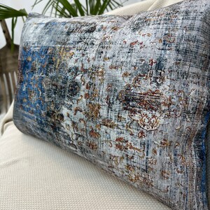 May include: A decorative throw pillow with a blue, gray, and gold patterned design. The pillow has a rectangular shape and is made of a soft, textured fabric.