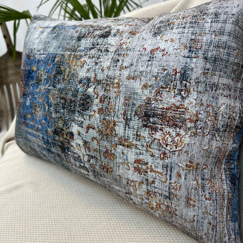 May include: A decorative throw pillow with a blue, gray, and gold patterned design. The pillow has a rectangular shape and is made of a soft, textured fabric.