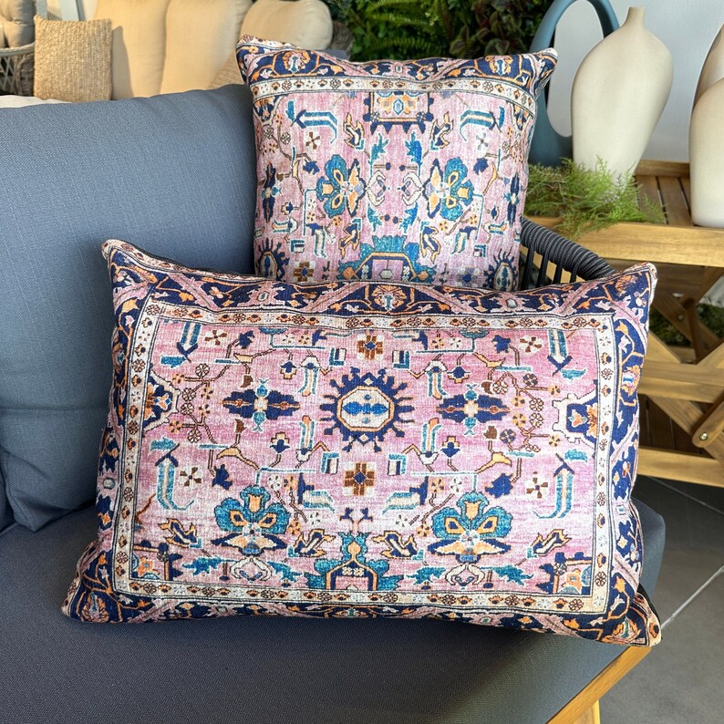 May include: Two decorative throw pillows with a vintage rug design. The pillows feature a pink background with a detailed pattern in navy blue, teal, and gold. One pillow is rectangular, and the other is square.