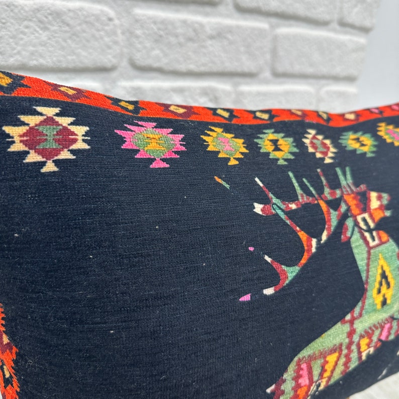 May include: Black pillow with a colourful geometric pattern and a stylised deer design. The pillow has a red, orange, yellow, green, pink and white border.