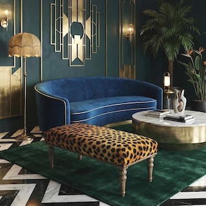 May include: A luxurious living room with a blue velvet sofa, a leopard-print bench, and a marble-topped coffee table. The room features gold accents, a green rug, and a patterned floor. A fringed floor lamp and decorative wall art add to the elegant decor.