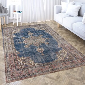Op de afbeelding: Een vintage-stijl tapijt met een blauwe achtergrond en ingewikkelde bloemmotieven in tinten rood, cr&egrave;me en bruin. Het tapijt heeft een verweerde uitstraling, waardoor het een unieke en antieke uitstraling heeft.