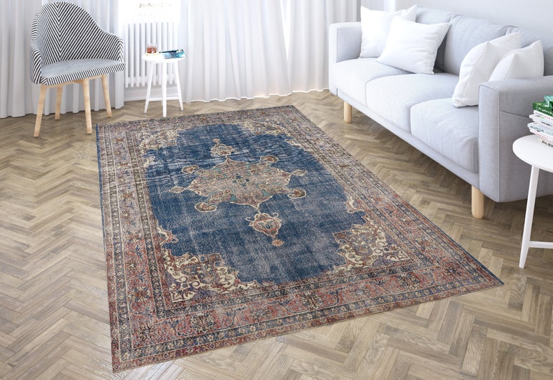 Op de afbeelding: Een vintage-stijl tapijt met een blauwe achtergrond en ingewikkelde bloemmotieven in tinten rood, cr&egrave;me en bruin. Het tapijt heeft een verweerde uitstraling, waardoor het een unieke en antieke uitstraling heeft.