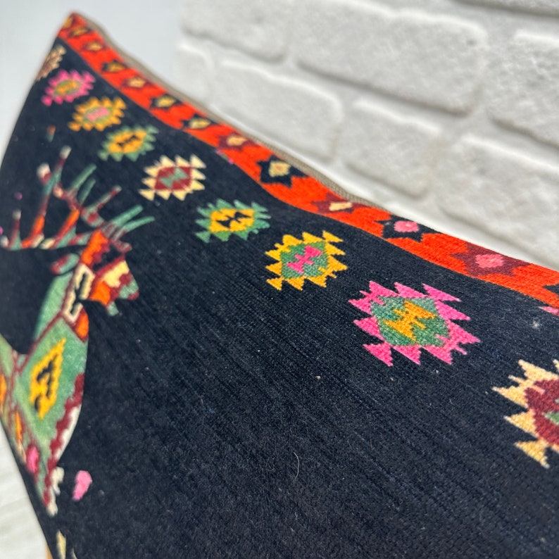 May include: Black throw pillow with a colourful geometric pattern and a stylised deer design. The pillow has a red, orange and yellow border.