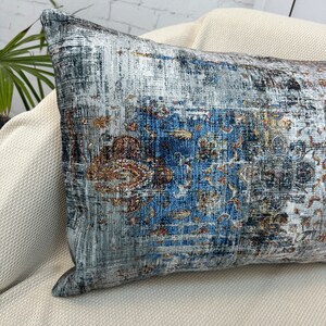 May include: A long rectangular throw pillow with a blue, gray, and gold abstract pattern. The pillow is made of a soft, textured fabric.