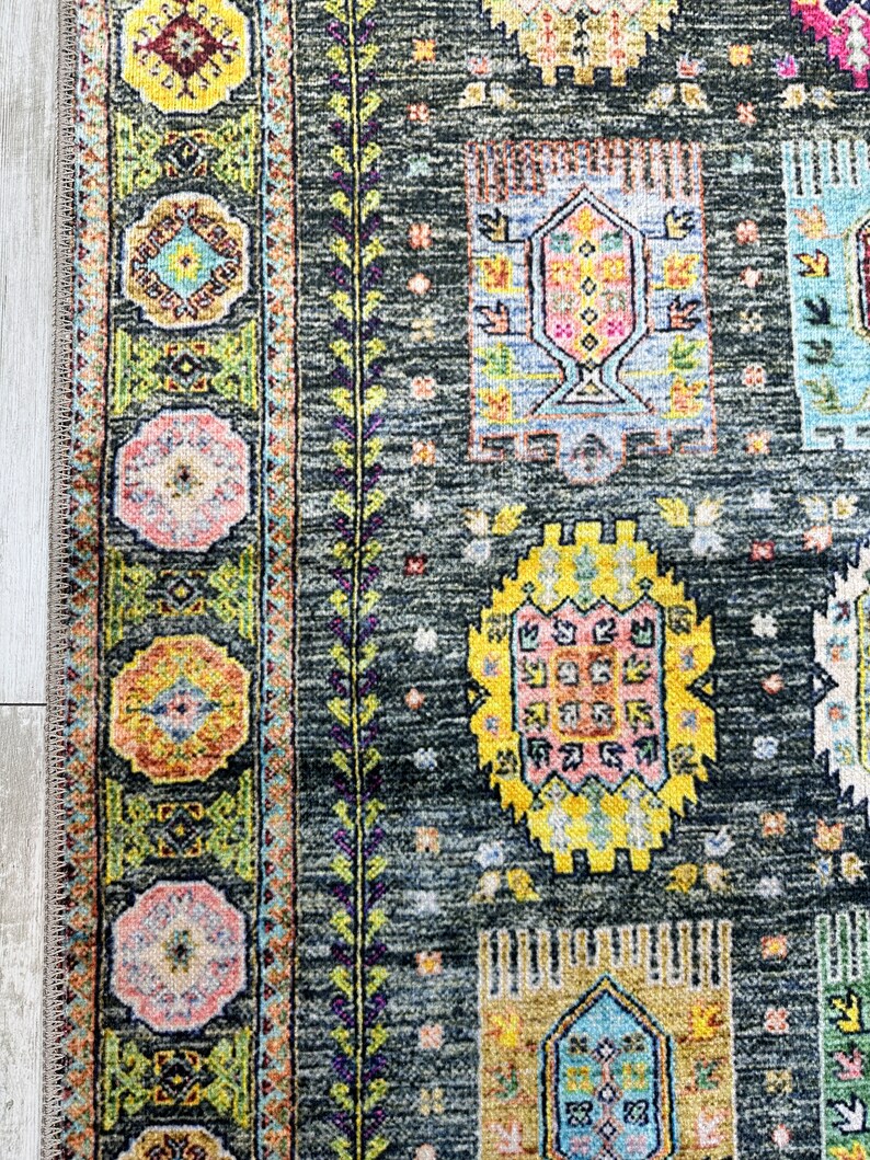 May include: A close-up of a dark gray rug with a colorful geometric pattern. The rug features a variety of shapes and colors, including yellow, pink, blue, and green. The rug has a fringe border.
